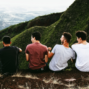 4 men sitting on a mountainside with their backs to the camera, laughing together