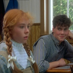 Anne Shirley (Megan Follows) looks concerned as Gilbert Blythe (Jonathan Crombie) looks on mischievously in their classroom (Anne of Green Gables)