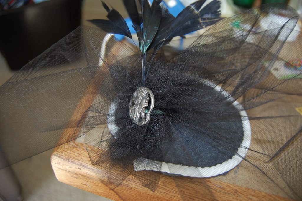 A dark gray fascinator with a silver broach and black tulle and feathers