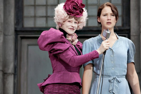 Screenshot from The Hunger Games, with Effie holding up the microphone to a dazed Katniss