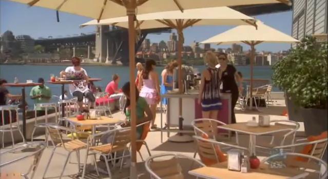 A cafe patio on the water with tables, chairs, and umbrellas