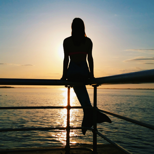 Silhouette of a mermaid sitting on a pier railing at sunset