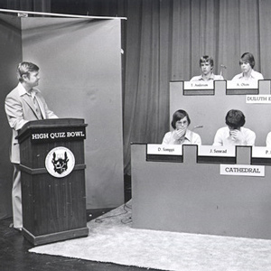 Teens behind a booth with microphones facing a moderator behind a podium