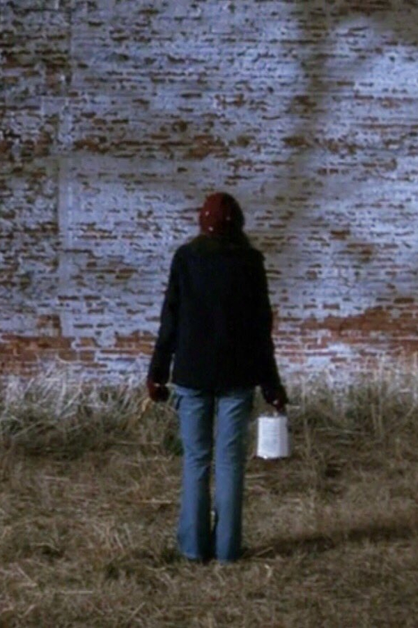 Joey stands in front of a blank wall at night, staring up at it with a paint bucket in her hand