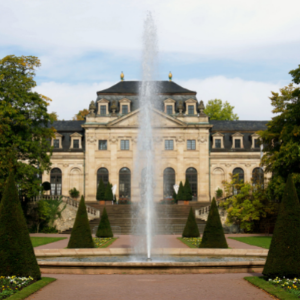 A big fancy mansion with a fountain and manicured trees in a large backyard