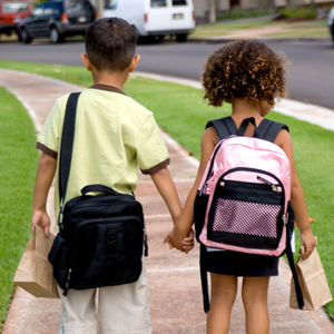 2 children wearing backpacks holding hands walking down the street