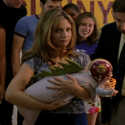 Buffy, looking slightly bewildered and holding a small pig wearing a football helmet and a fake razorback