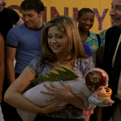 Buffy, looking slightly bewildered and holding a small pig wearing a football helmet and a fake razorback