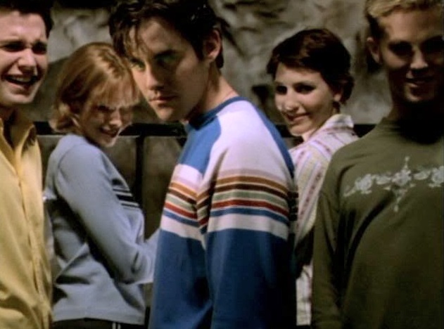 Xander, standing with a group of four teens who are all sneering and laughing as he looks towards the viewer with a dangerous glint in his eye