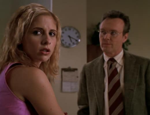 Buffy with clipped back crimped hair stands with Giles in the library