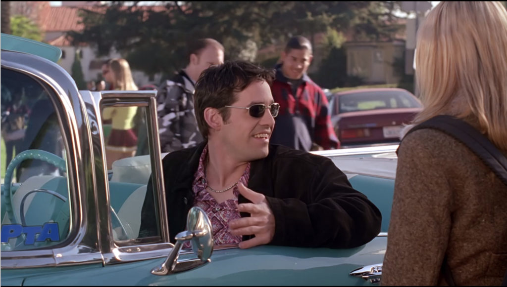 Xander wearing sunglasses and driving a vintage convertible