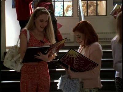 Harmony and Willow sign yearbooks while Willow carries a purse covered in light blue fur