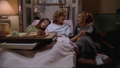 Dawn cuddles up next to Joyce in her hospital bed, while Buffy holds Joyce's hand