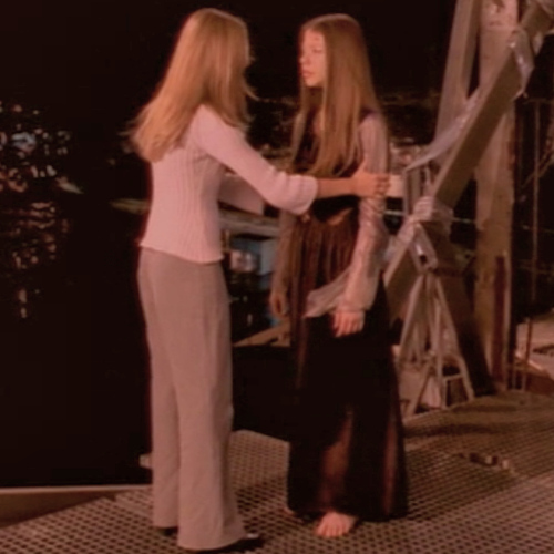 Buffy holds Dawn's arms as they stand on the top of the tower.