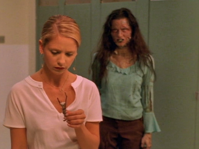 A ghost stands behind Buffy examining a totem while they're in the school bathroom. 