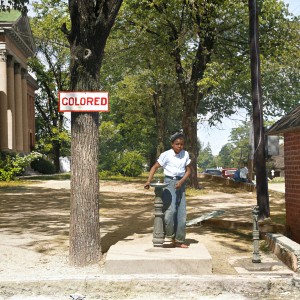 A Black boy drinking at a water fountain with a "Colored" sign