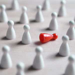 Little white game pieces standing around by a red game piece lying on its side