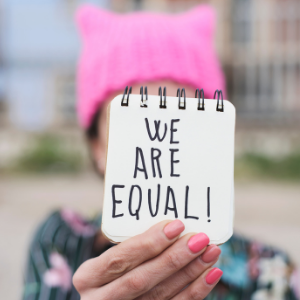 Woman from the Women's March wearing a pink pussy knit hat holding notepad saying "we are equal!"