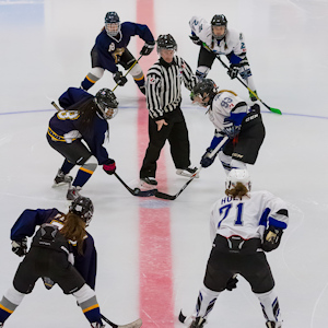 Hockey referee standing between 3 vs 3 hockey players facing off 