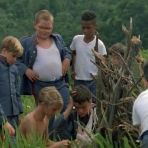 Young boys standing around a pile of sticks trying to start a fire from the movie Lord of the Flies