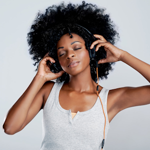 Beautiful african woman with afro listening to music with eyes closed in studio