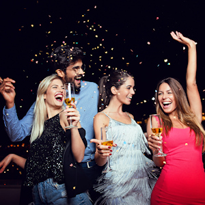 4 people in fancy clothes holding champagne and laughing as confetti flies in the air