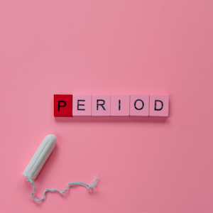 The word PERIOD spelled in scrabble tiles next to a tampon on a pink background