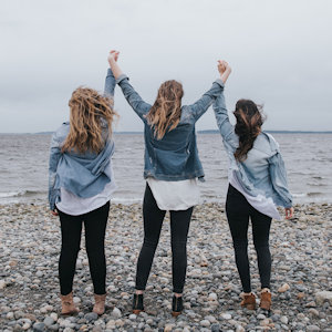 Three women on a beach holding hands in the air triumphantly