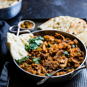 Bowl of Indian food with naan bread next to it