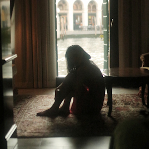 Silhouette of a woman sitting sadly on the floor in front of a balcony