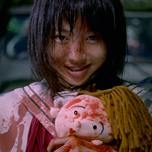 A little Japanese girl, splattered in blood, smiling and clutching a stuffed animal
