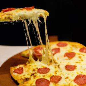 Pizza slice with stringy cheese still attached to the pie