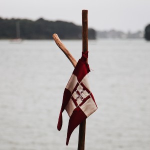 A white and maroon flag tied to a stick stuck on the beach of a lake