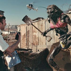 Scene from District 9 with an alien wearing a pink bra and waving a shovel at a human