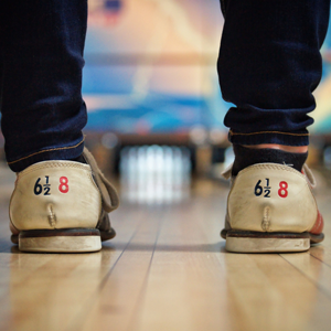 Two feet wearing bowling shoes standing in front of a bowling alley