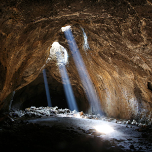 A cave with an opening in the top where the sunlight is shining down