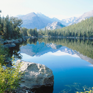 A lake surrounded by greenery and the Colorado Rocky Mountains