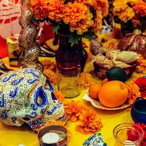 Colourful ofrenda with a calavera, vase of flowers, plate of oranges, candles, and other decorations