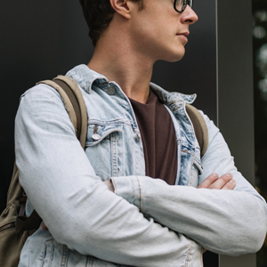 Guy in denim jacket with glasses and backpack crossing his arms