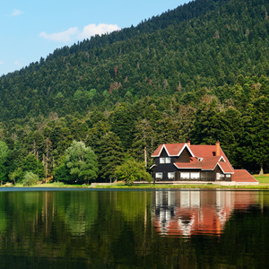 A black house with a red roof on the edge of a lake surrounded by mountains