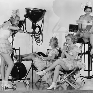 Old timey female extras relaxing on a movie set surrounded by lighting rigs