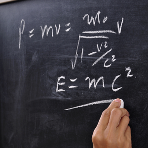Blackboard with a hand writing a physics equation E=mc2