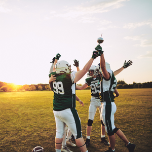 A group of American footballers jumping and cheering in a field at sunset