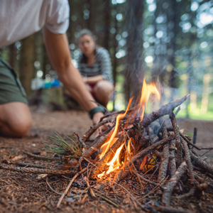 A person leaning over a campfire built with sticks