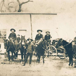 Old timey photo of people from the 1800s West, sitting on horses and with wagons