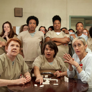 Various prisoners in tan prison jump suits watching TV from Orange is the New Black