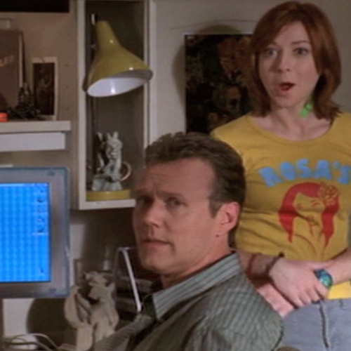 Giles sits at a computer while Willow stands behind and makes a knowing face.