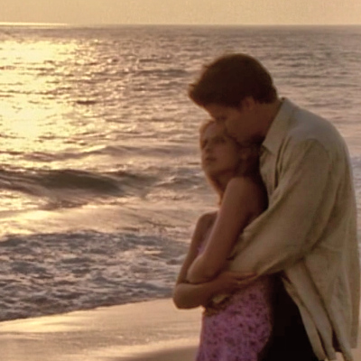 Buffy and Angel cuddling on the beach at sunset.