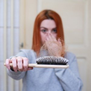 A girl looking in horror at a hairbrush filled with an unusual amount of hair