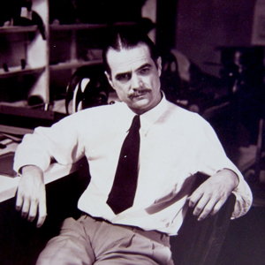 Howard Hughes, wearing a tie and reposing in a chair